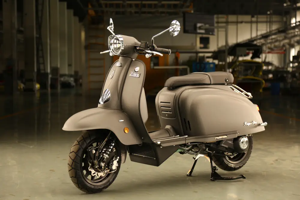 Ein Retro-Motorroller von Royal Alloy in einer dunklen Halle. Das Fahrzeug ist in einer eleganten, matten Farbgebung gehalten.